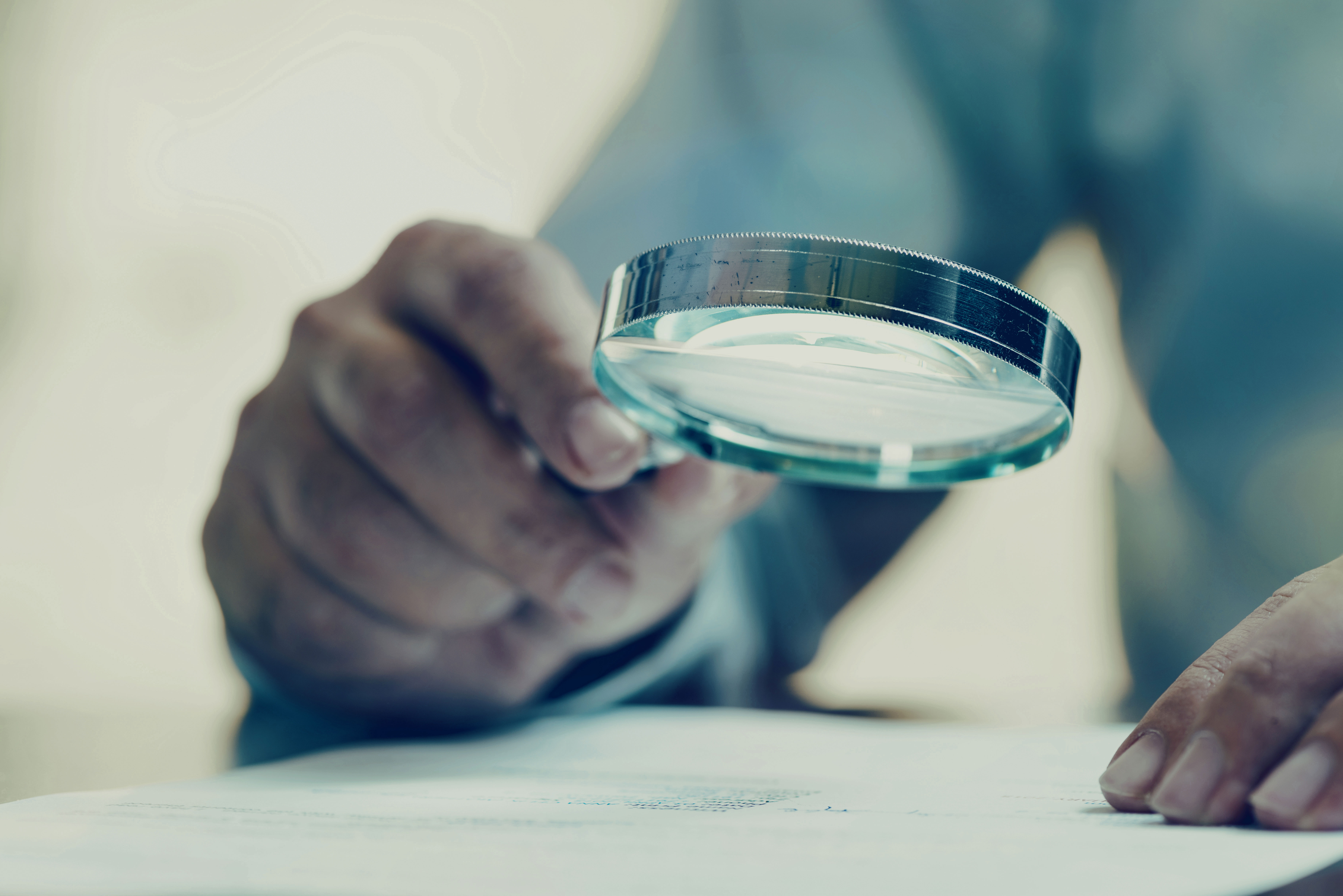 A person holding a magnifying glass over paper